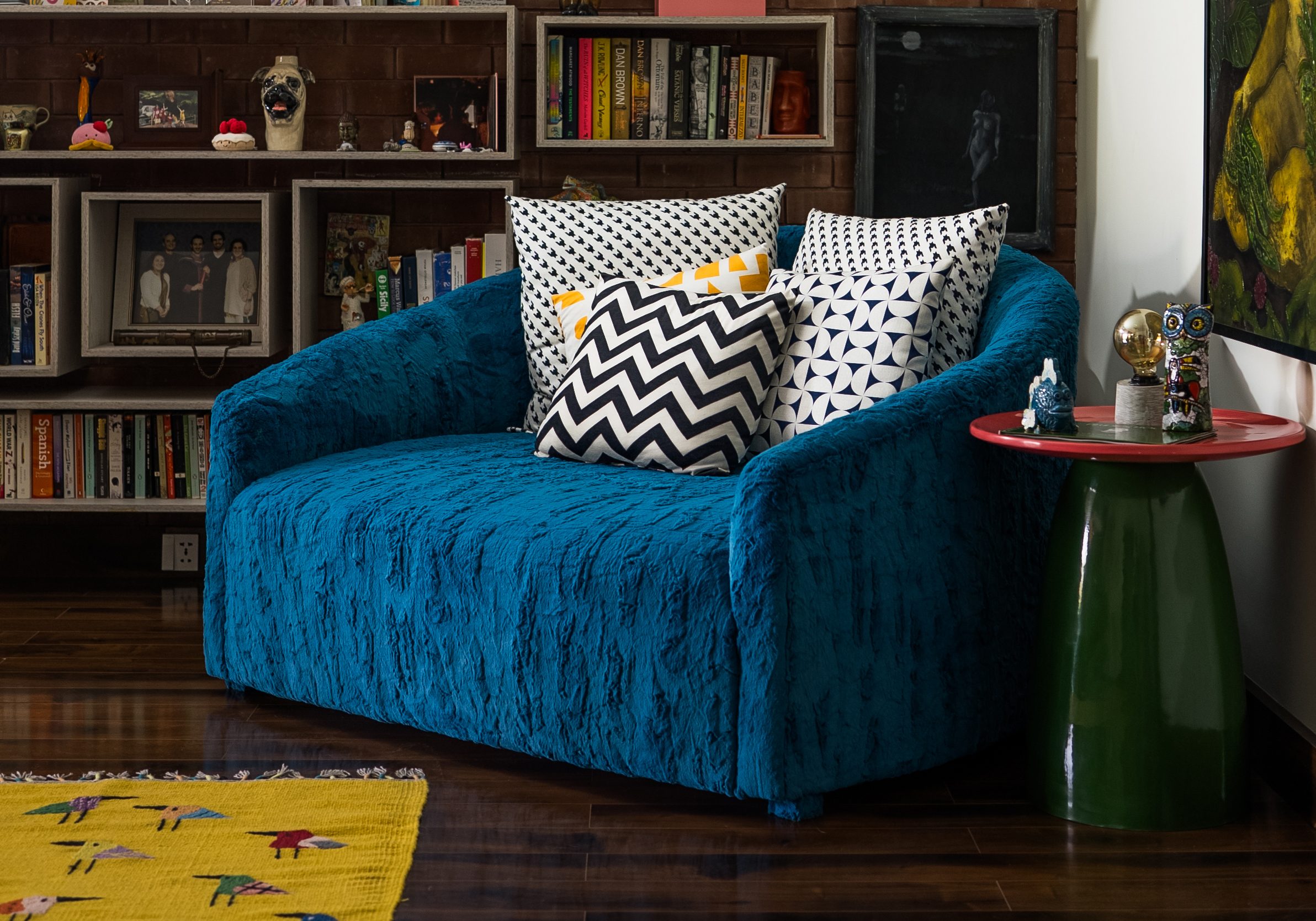 Library and display shelving above a blue velvet sofa