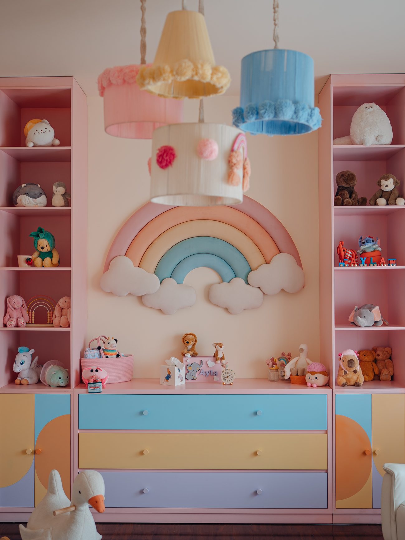 Pastel nursery with a padded rainbow, colour-blocked drawers and pompom pendant shades