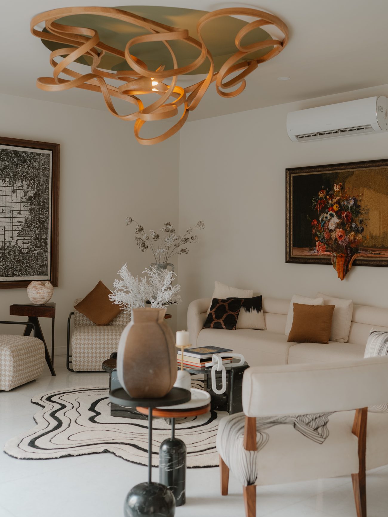 Pale lounge beneath the carved Raka light, with a stone vase on black marble tables and a contour rug