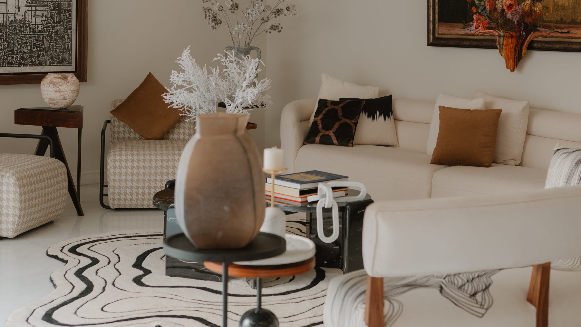 Pale lounge beneath the carved Raka light, with a stone vase on black marble tables and a contour rug