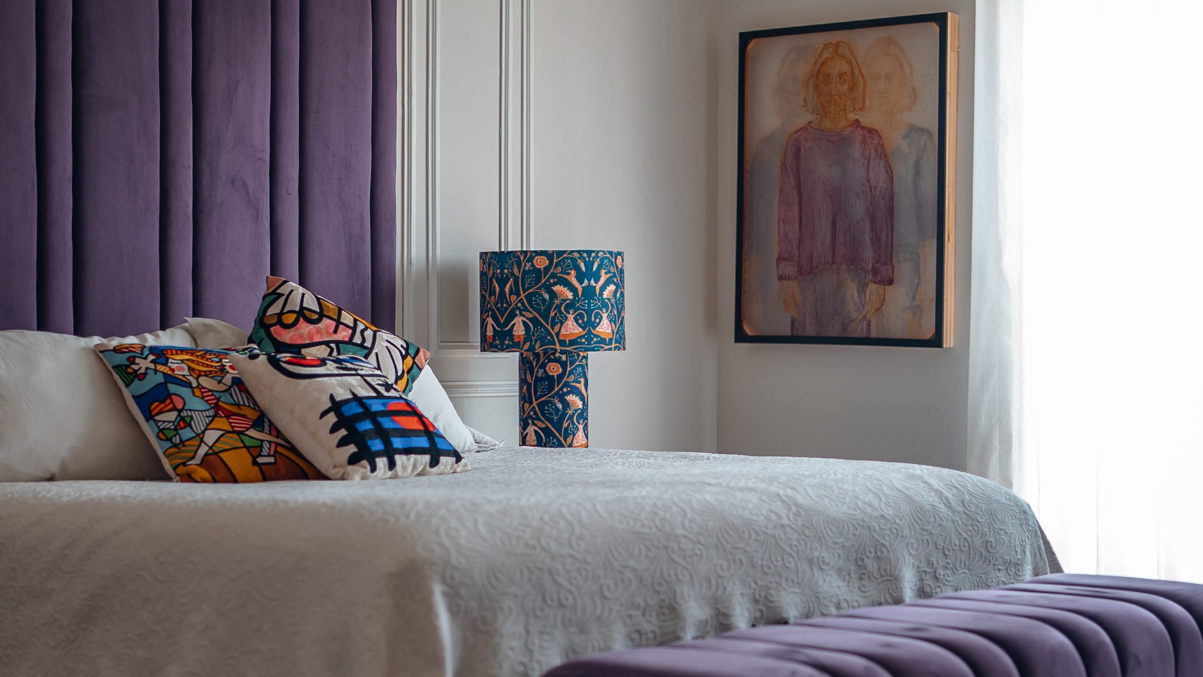 Bed with a purple channel-tufted headboard and matching bench, white bedding and patterned cushions