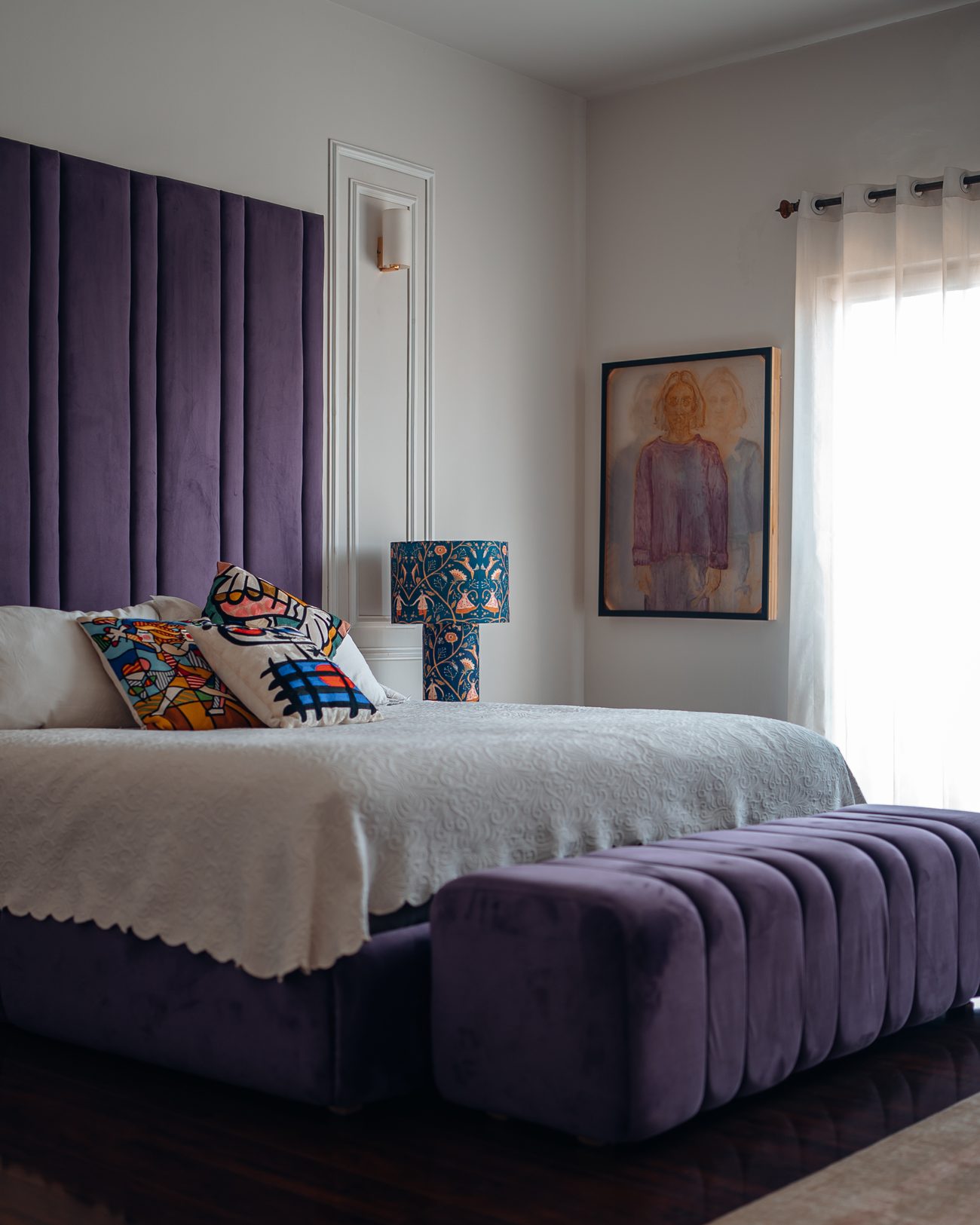 Bed with a purple channel-tufted headboard and matching bench, white bedding and patterned cushions
