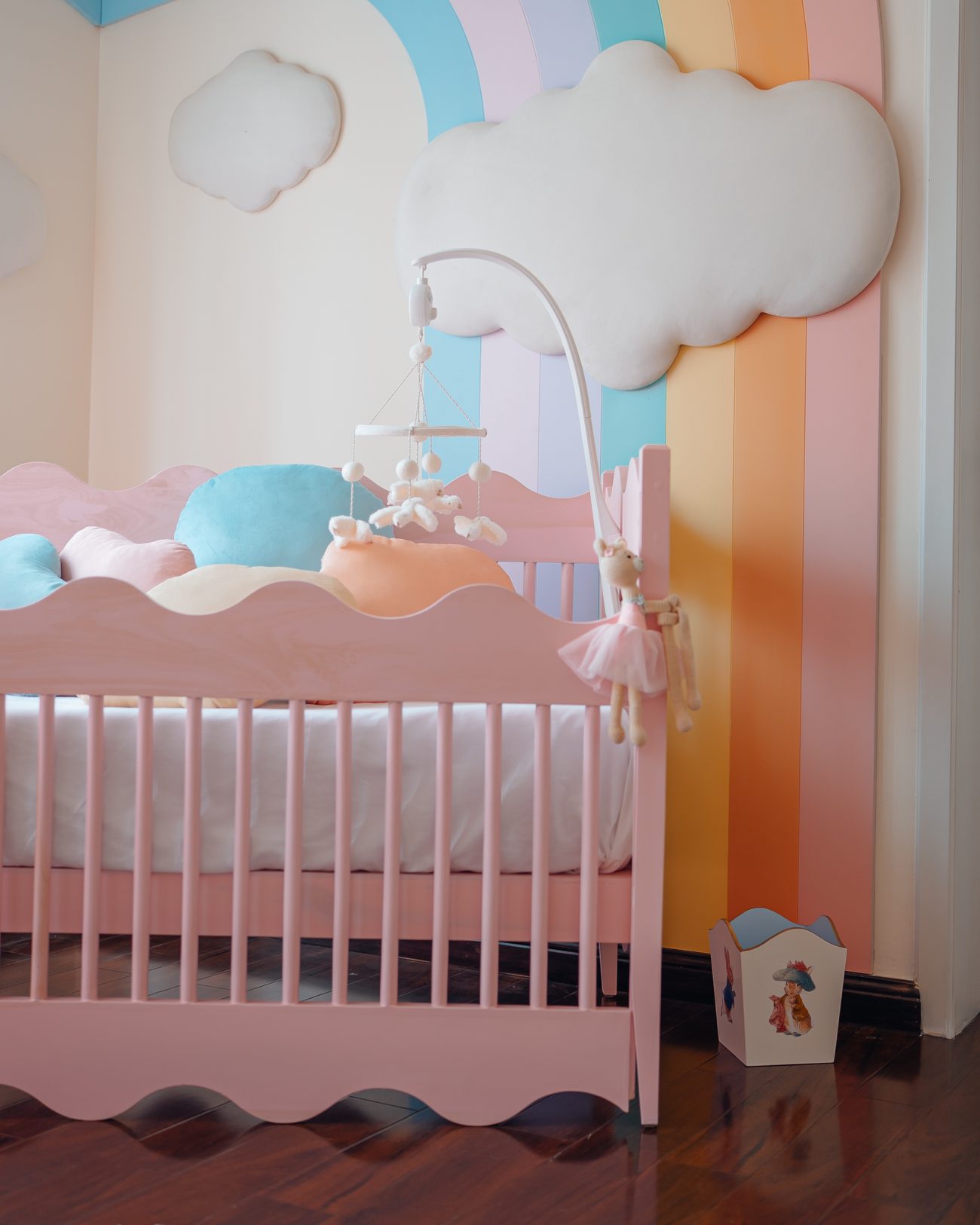 Pastel nursery with a padded rainbow, colour-blocked drawers and pompom pendant shades